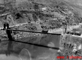 Trucks wait to cross a bridge on the Salween River one at a time. Note how the bridge bends down under the load of the transport truck going across. During WWII.
