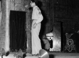 A GI stands at the microphone during entertainment of the CBI, as the Jive-o-Lieps are ready at their instruments. During WWII.