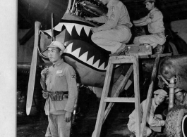 A Curtiss P-40 is being serviced by Sgts. Bloom, Dull, Yaranow, and Baker, while a Chinese soldier stands guard.