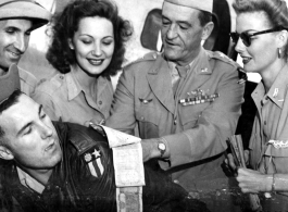 Chennault signs a "short-snorter" bill in the CBI while Hollywood stars look on--Ann Sheridan, Ben Blue, and Mary Landa.