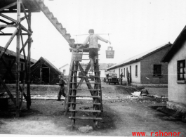 Worker fills water tank at an American base in Yunnan, China, during WWII, by climbing up stairs carrying pails of water.