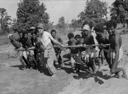 To get a great photo, a GI lends a hand to Indian work crew to pull concrete roller.  Scenes in India witnessed by American GIs during WWII. For many Americans of that era, with their limited experience traveling, the everyday sights and sounds overseas were new, intriguing, and photo worthy.