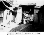 Village street in Yunnanyi, China, during WWII, with gate having a sign for Shanghai Man Hairstyling (上海男美发室), and the Almond Flower Tea Room (杏花茶室）in the shadow on the right. 1944.