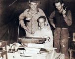 "Jim Kruger (standing), Elliot Knecht (seated), and an unknown member of the 396th having their picture taken in the Orderly Room."