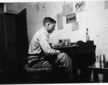 View inside barracks for two GIs in Yunnan, China, during WWII--GI at desk.
