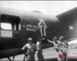Men pose next to artwork of the tail of B-24 "Open For Business" of the 308th Bombardment Group.