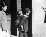 Older brother carries younger brother in a Chinese town during WWII. 