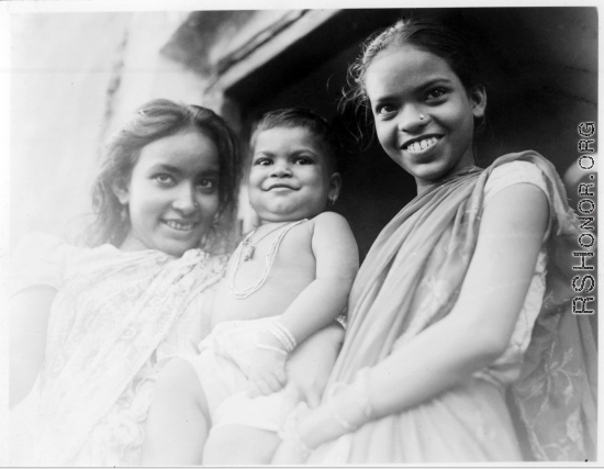 Older sisters hold pride and joy brother.  Scenes in India witnessed by American GIs during WWII. For many Americans of that era, with their limited experience traveling, the everyday sights and sounds overseas were new, intriguing, and photo worthy.