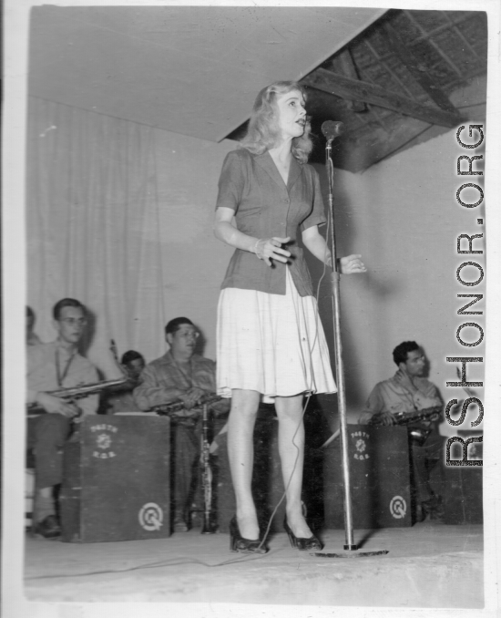 Singer at a USO show in Gushkara, India, during WWII.  The boxes in front of the band players are labeled 748th ROB (748th Railway Operating Battalion).