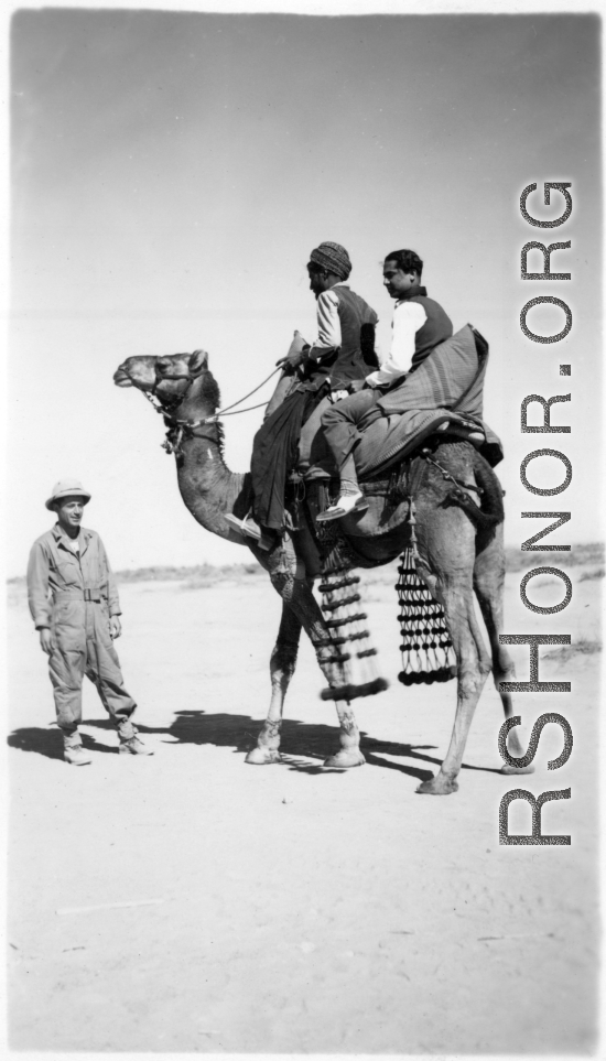 Men ride camel as a GI looks on.  Scenes in India witnessed by American GIs during WWII. For many Americans of that era, with their limited experience traveling, the everyday sights and sounds overseas were new, intriguing, and photo worthy.