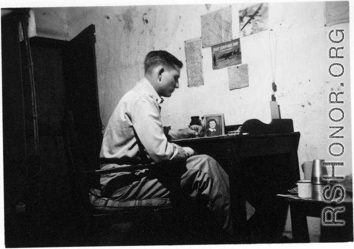 View inside barracks for two GIs in Yunnan, China, during WWII--GI at desk.