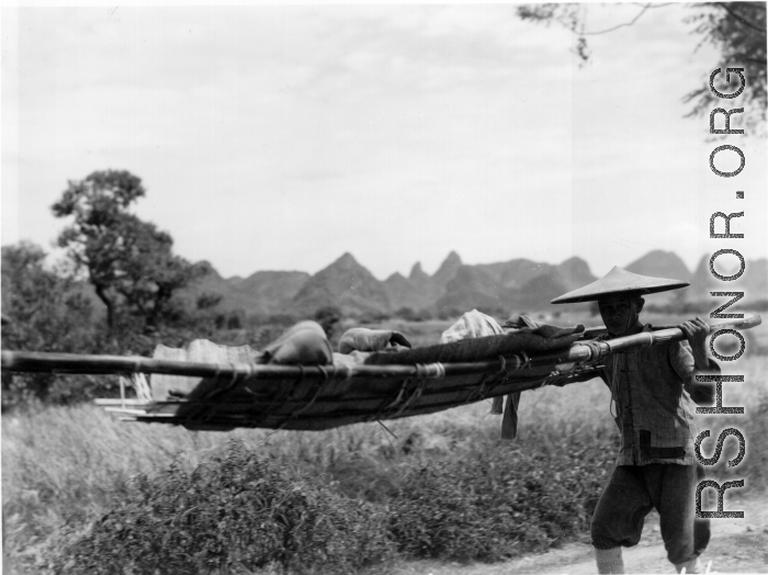 Men shoulder stretcher with injured or sick person in Guangxi, China, during WWII.