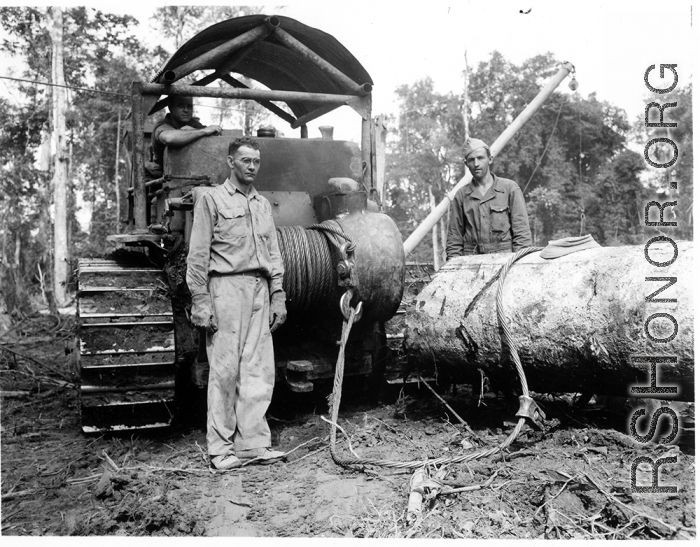 Bulldozer using cable choker to pull log through mud in Burma.  797th Engineer Forestry Company in Burma.  During WWII.