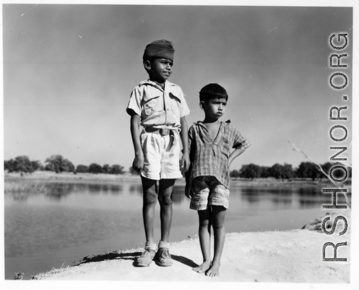 Two boys pose side by side, one in a scout uniform or similar.  Scenes in India witnessed by American GIs during WWII. For many Americans of that era, with their limited experience traveling, the everyday sights and sounds overseas were new, intriguing, and photo worthy.