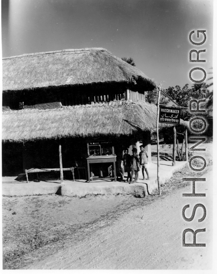 Local kids hang out at a thatched-roofed building advertising "Watch Maker."  Scenes in India witnessed by American GIs during WWII. For many Americans of that era, with their limited experience traveling, the everyday sights and sounds overseas were new, intriguing, and photo worthy.