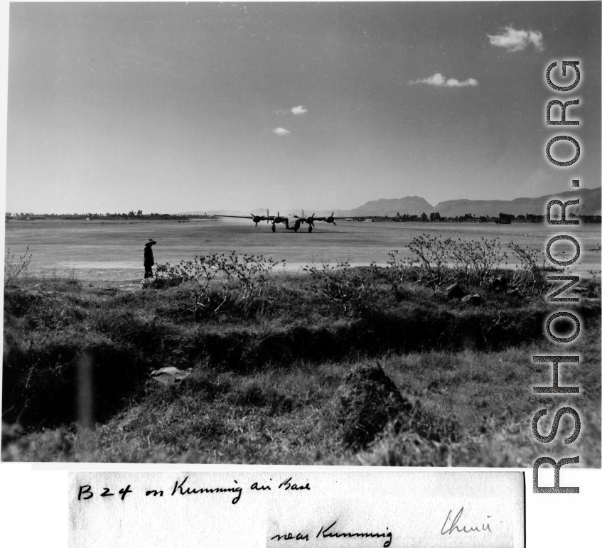 B-24 stirs up dust on runway at Kunming, China, during WWII. Chinese worker stands in the foreground, as well as some in the far distance.