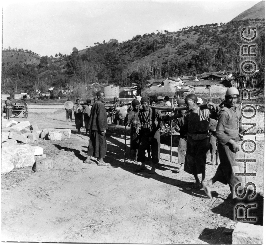 Laborers in a rural location in SW China carry larges timbers. During WWII.