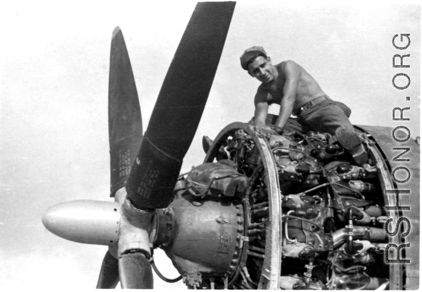 An American aircraft mechanic doing maintenance sits astride a large aircraft engine. In the CBI during WWII.