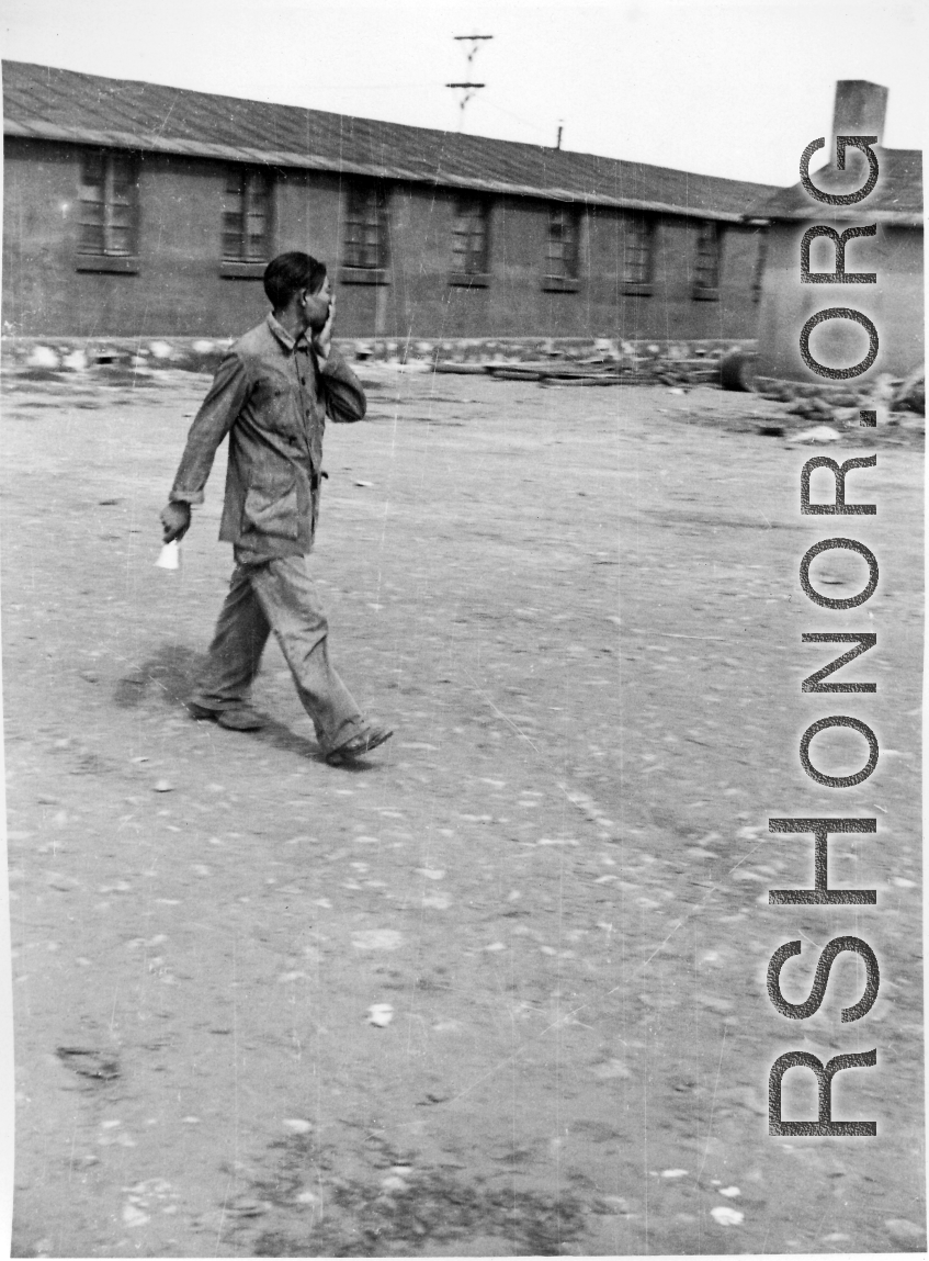 A Chinese staff person walks across an open area of a hostel in Yunnan province, China, most likely around the Luliang air base area.