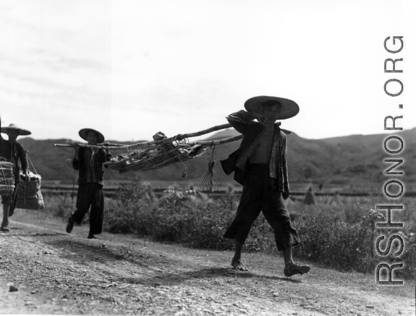 Men shoulder a stretcher, possibly carrying recovered human remains. During WWII, in China.