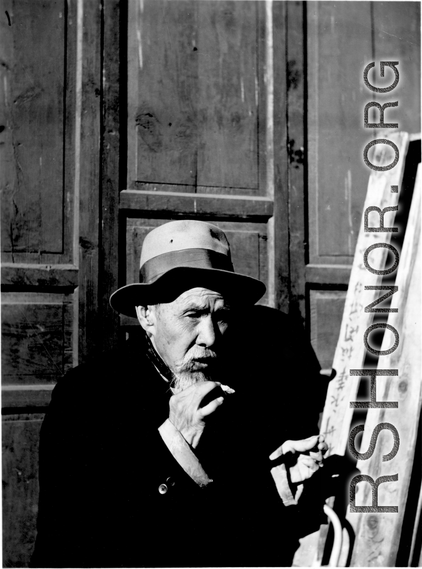 An elderly Chinese man in Liuzhou (based on the inverted sign behind him) smokes a cigarette during WWII.