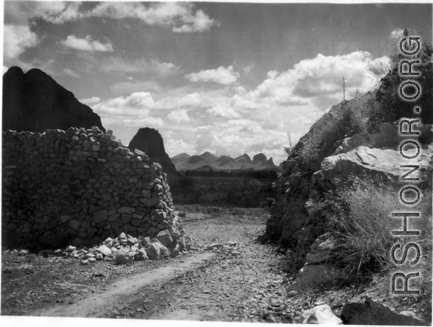 Karst mountains in the distance seen through an opening in a wall of stacked limestone. In Liuzhou, Guangxi, during WWII.