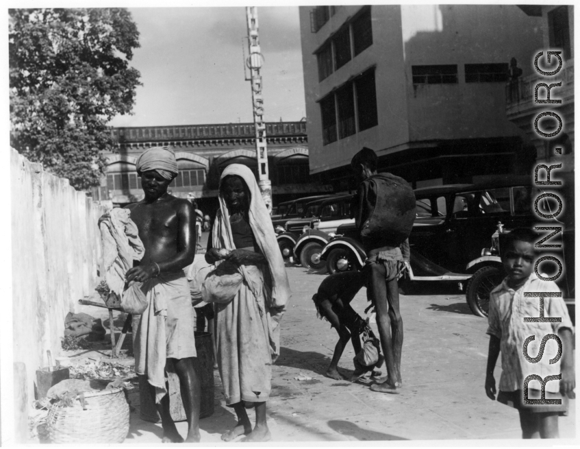 Poor people on street next to nice cars.  Scenes in India witnessed by American GIs during WWII. For many Americans of that era, with their limited experience traveling, the everyday sights and sounds overseas were new, intriguing, and photo worthy.