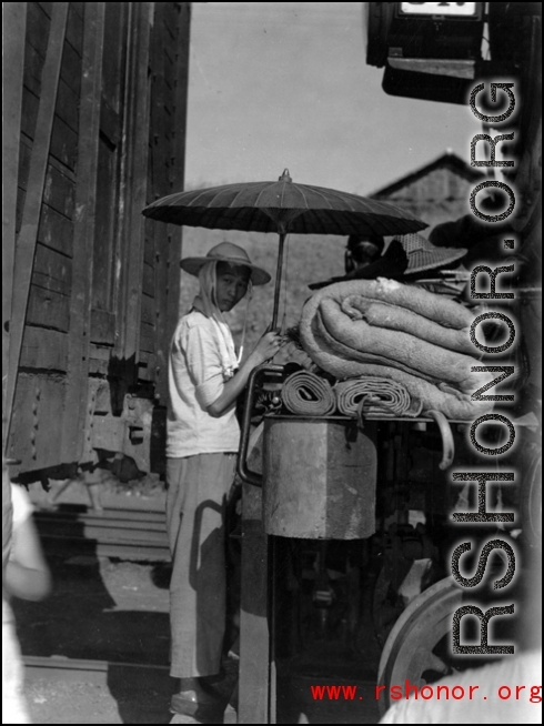 A Chinese refugee making shade from the hot sun between train cars. At the train station in Liuzhou during WWII, in the fall of 1944, as the Japanese advanced during the Ichigo campaign.