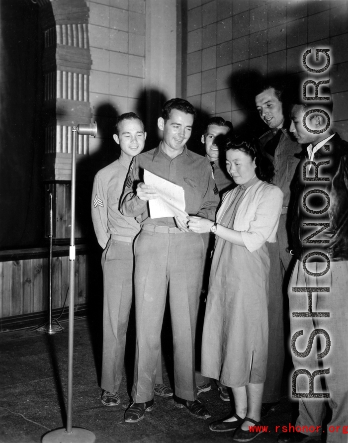 A group of Americans and two Chinese prepare to sing off a sheet of paper into a microphone.