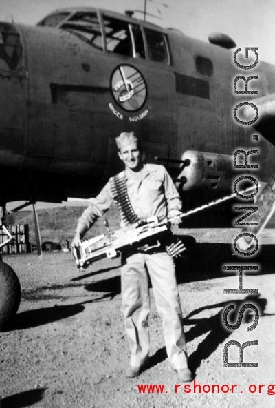 Robert Fox holds a heavy machine gun in front of a B-25 of the Ringer Squadron.