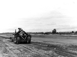 Mechanical grader flattens out a runway in the CBI during WWII, while C-47 moves in the background.