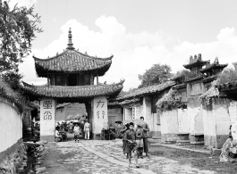 A whitewashed village street in Luliang, Yunnan, China, with a small gate tower towards the left, and ceremonial arch on the right. Local people in China.