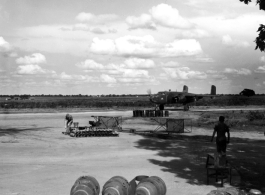 A B-25D of the American 491st Bombardment Squadron is on the taxiway.  Maintenance men who prepared it for the mission stand in the shade of tree. Small bombs, 100 pounds, are seen neatly stacked in the middle of the photo. Closer, in the center, are three 500 pound bombs. They lack the guide fins, and still have the transport 'rings' attached to make it easier to move them around.  Photo believed to have been taken at Yangkai, Yunnan Province, in the spring or summer of 1944. 