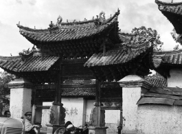 Men waiting near a memorial archway. Local people and architecture in Yunnan province, China, during WWII.