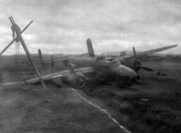 A B-25 in the ditch next to a runway or taxiway at an American base in China, during WWII. Crews work to salvage the aircraft using a simple human-powered tripod crane.