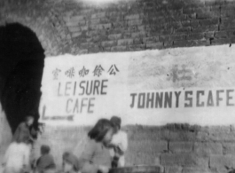 Signs in English for the "Leisure Cafe' (公余咖啡室) and "Johnny's Cafe painted on a town wall near a town gate in China during WWII.