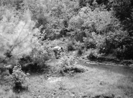 An American soldier fusses over something near a stream in Yunnan province, China, during WWII.