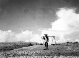 A farmer or laborer in China posing with a should pole. During WWII. Notice the freshly spread stone in the foreground, almost certainly crushed by hand, then hauled to the location by hand (for example, using shoulder poles), then spread and tamped down by human labor.