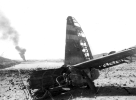 An American airplane destroyed after a Japanese air raid, with another burning in the distance. In China, during WWII.