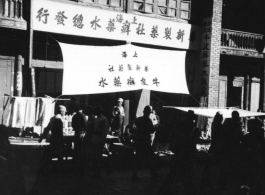 A large sign advertises for psoriasis lotion (牛皮癣水), and touts call out to passers-by in China. During WWII.  From the collection of Hal Geer.