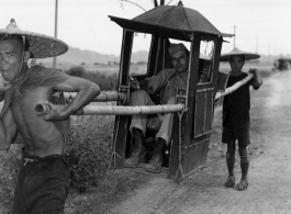 GI rides a sedan chair carried on bamboo poles by two Chinese men. During WWII.