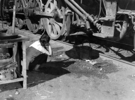 Chinese refugee waits with a bucket for hot water to drip from a steam train engine at the train station in Liuzhou during WWII, in the fall of 1944, as the Japanese advanced during the Ichigo campaign.