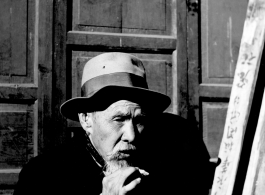 An elderly Chinese man in Liuzhou (based on the inverted sign behind him) smokes a cigarette during WWII.