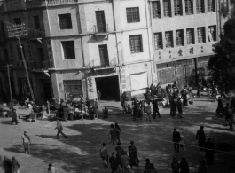 Scenes around Kunming city, Yunnan province, China, during WWII: Corner with curbside sellers and cloth market.