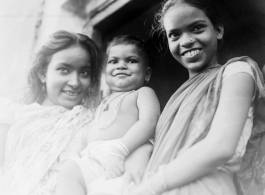 Older sisters hold pride and joy brother.  Scenes in India witnessed by American GIs during WWII. For many Americans of that era, with their limited experience traveling, the everyday sights and sounds overseas were new, intriguing, and photo worthy.