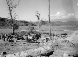 Site at the mill yard, including a large log heading towards saw at a lumber mill of the 797th Engineer Forestry Company in Burma. Sawdust flys through pipe onto large pile.  During WWII.