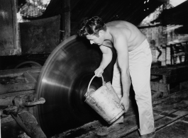 GI of the 797th Engineer Forestry Company in Burma, dousing spinning deadly saw blade with water, for cooling or cleaning.  During WWII.