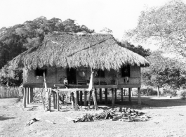 A woman sitting on the porch of a thatched-roof house on stilts in Burma.  Local people in Burma near the 797th Engineer Forestry Company.  During WWII.