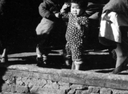 Two toddlers hang out while the adults drink tea at roadside location. In China, during WWII.