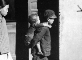 Older brother carries younger brother in a Chinese town during WWII. 